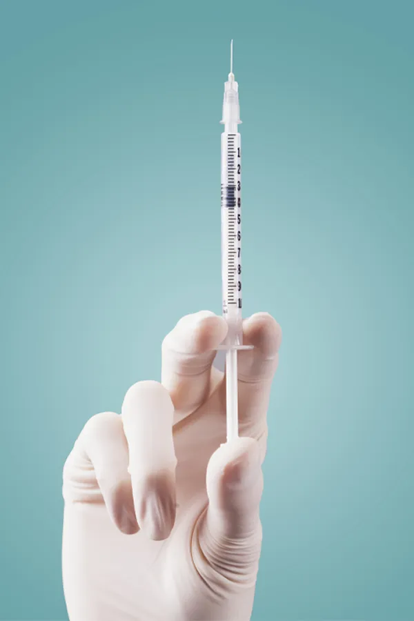 Aesthetic-Fillers-Treatment Close-up of a white-gloved hand holding a syringe against a light blue background, representing aesthetic filler services from Genifer Chavez, MD in Tucson.