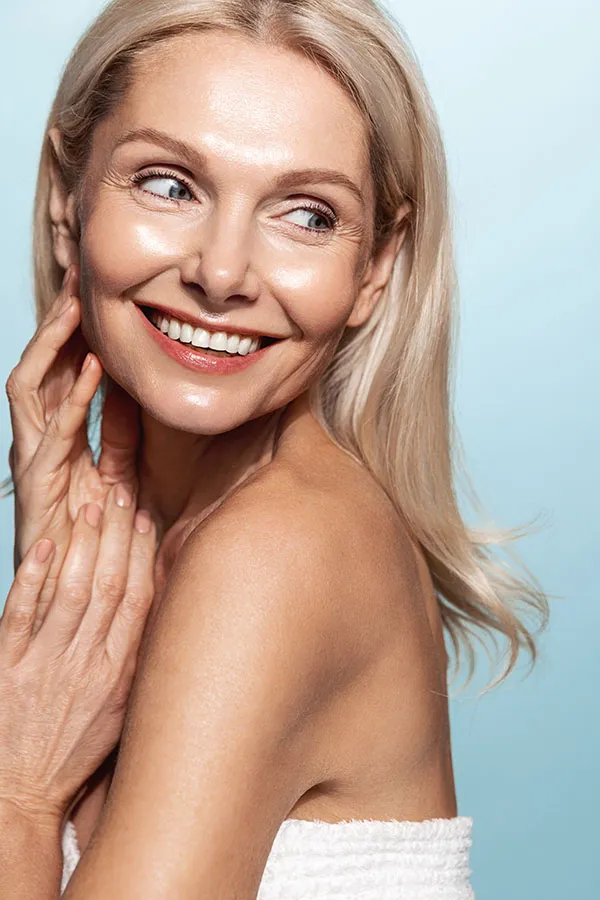 PDO-Threads-Treatment An older blonde woman touches her face to feel the beautiful results of her PDO thread lift treatment from Genifer Chavez, MD in Tucson.