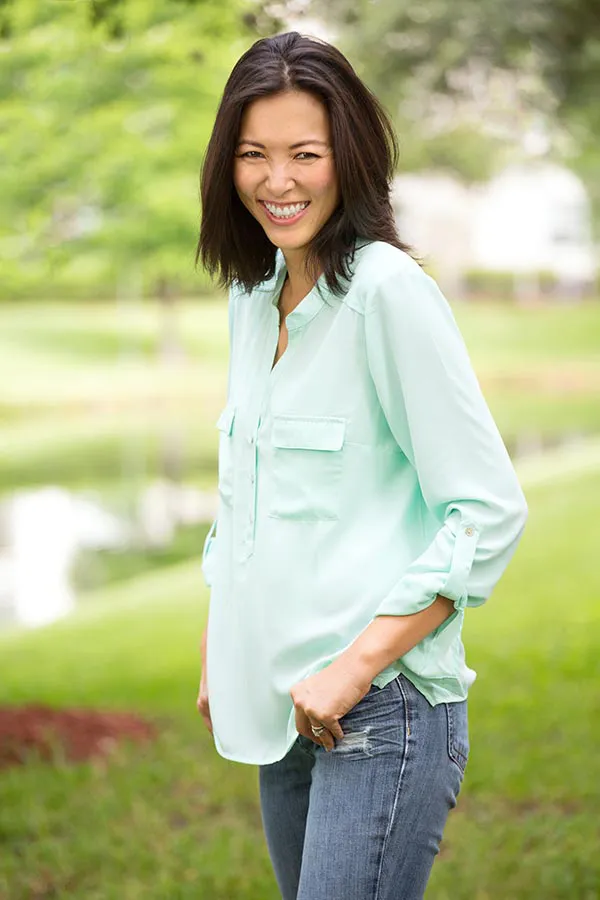 Perimenopause-Treatment A middle-aged brunette woman in a light green button-up shirt stands outside smiling, happy with her perimenopause treatment from Genifer Chavez, MD in Tucson.